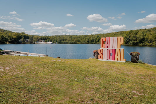Lakeside view at an adult sleepaway camp with a large Camp Social sign