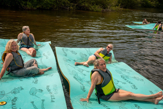 Women relaxing on lake floats at adult summer camp by Camp Social