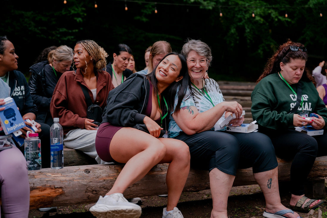 Campers of all ages laughing together on log benches at Camp Social