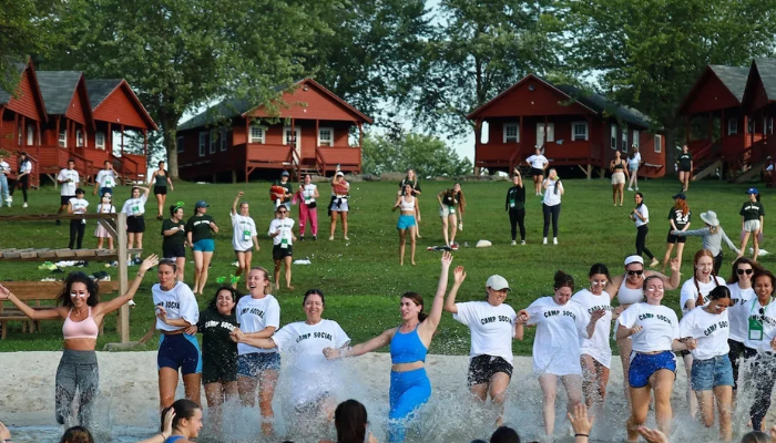 Women walking into a lake in front of cabins at Camp Social